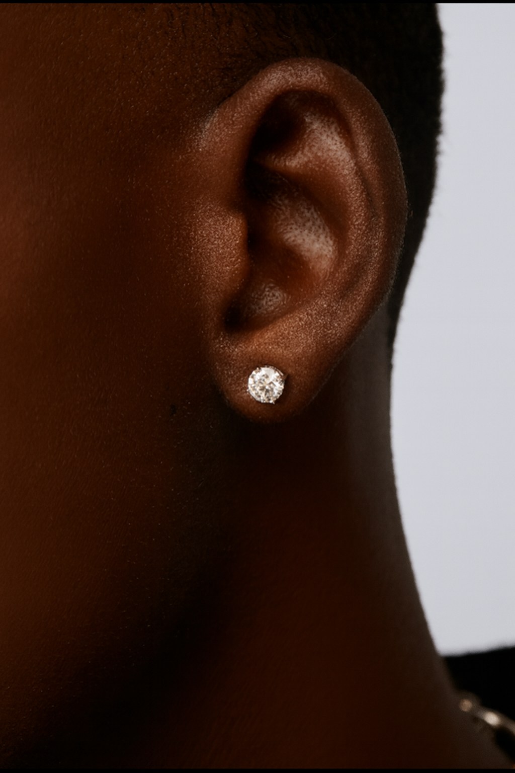 Close-up of an ear wearing a diamond stud earring with a neutral background