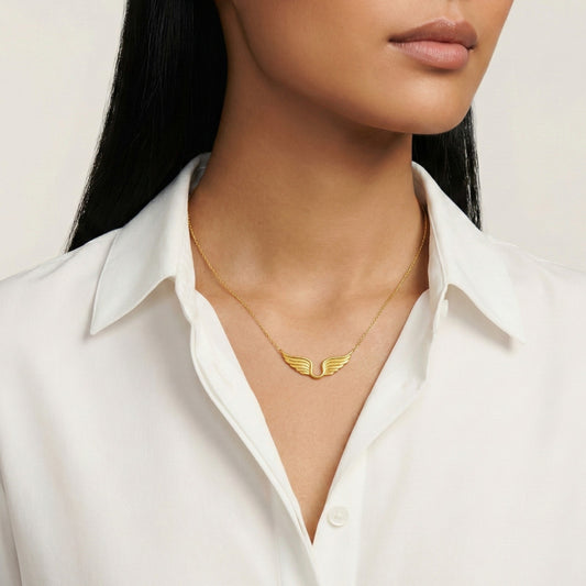 Gold wing-shaped necklace worn by a person in a white shirt