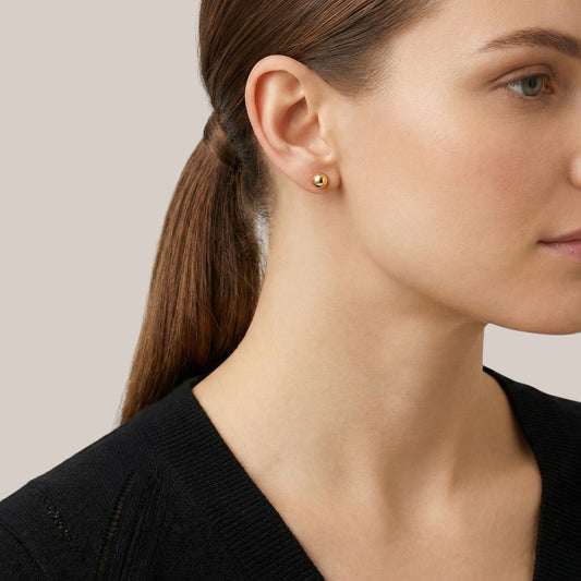 Close-up of a woman wearing gold earrings with a neutral background