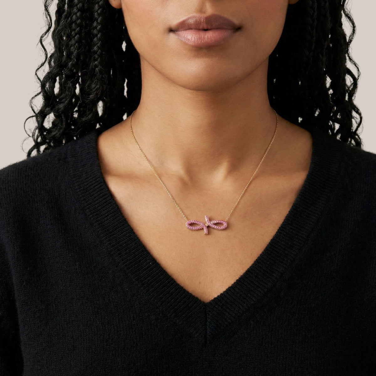 Necklace with a pink pendant worn by a person against a neutral background