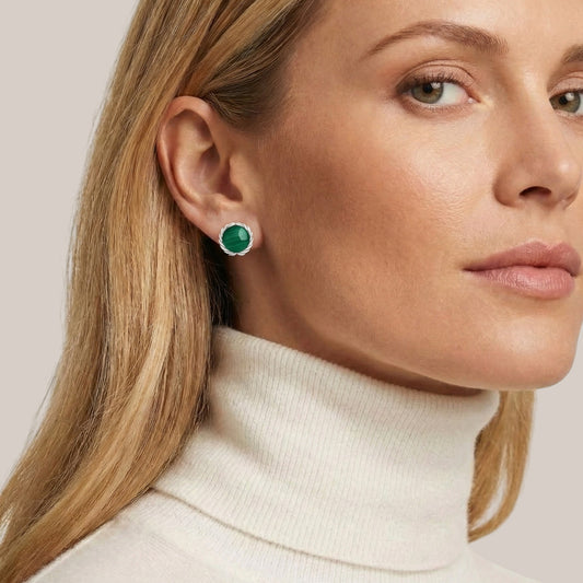 Close-up of a woman wearing green gemstone earrings with a neutral background