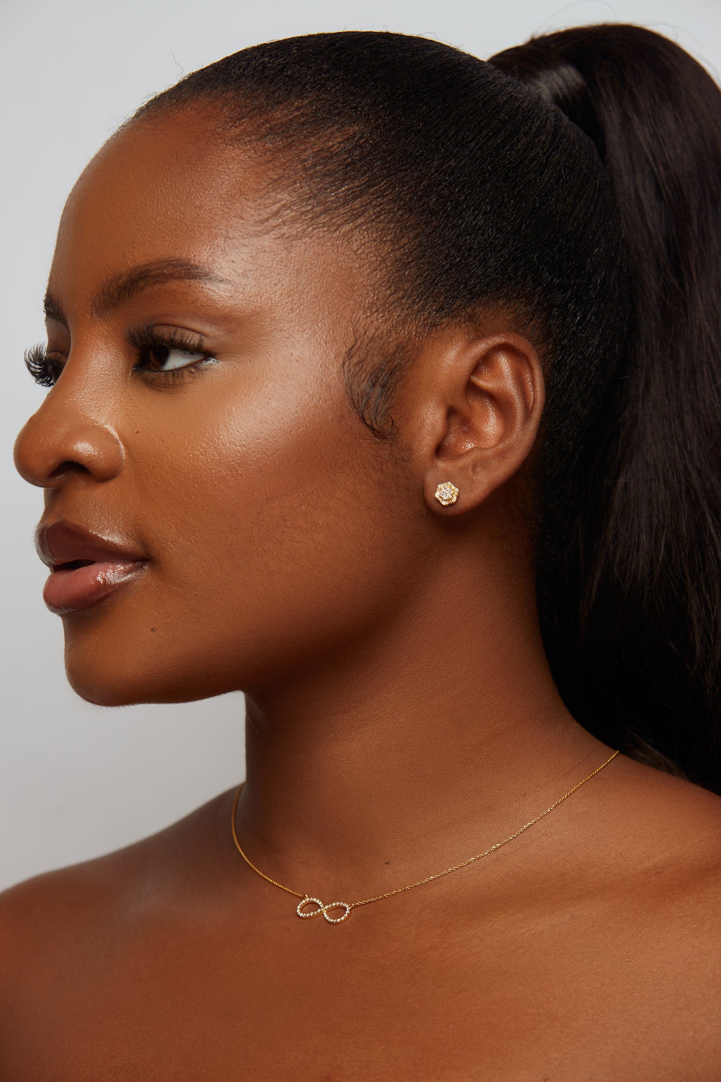 Woman wearing a gold necklace with an infinity symbol on a plain background