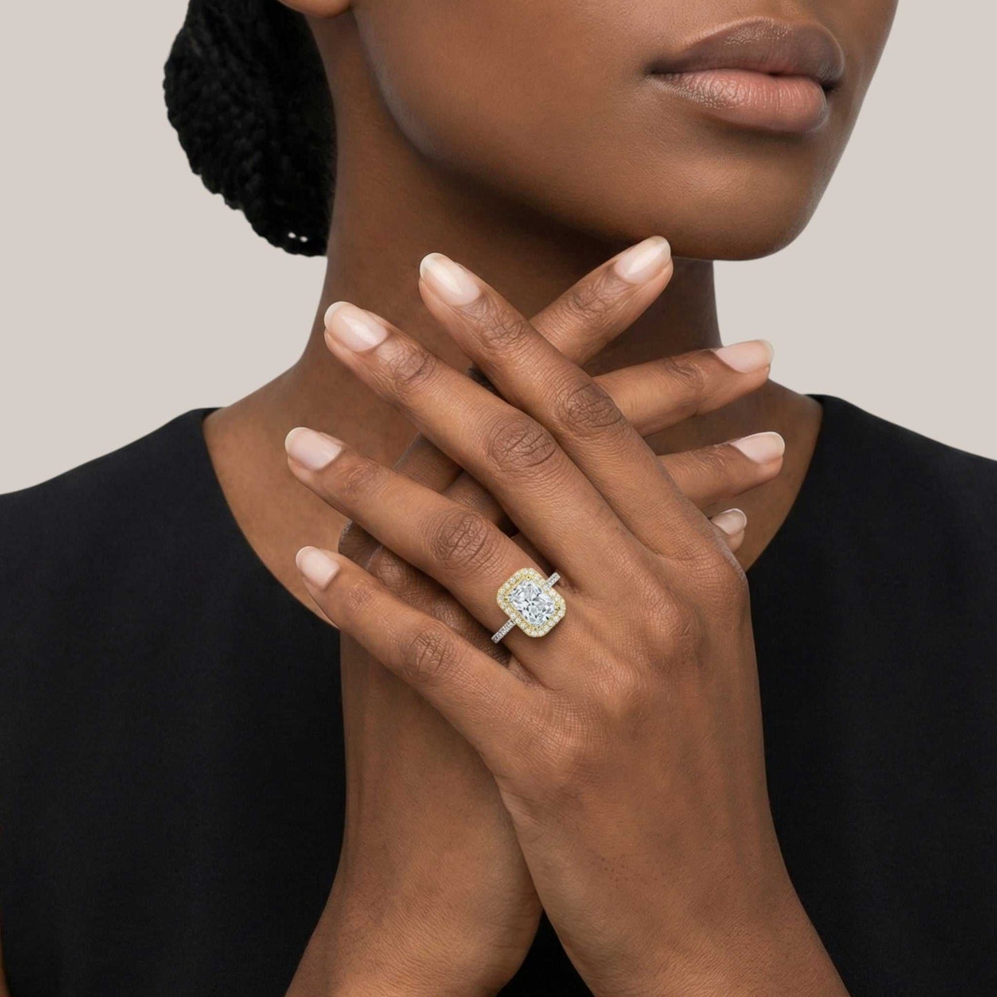 Woman wearing a gold ring with a diamond on her finger against a neutral background
