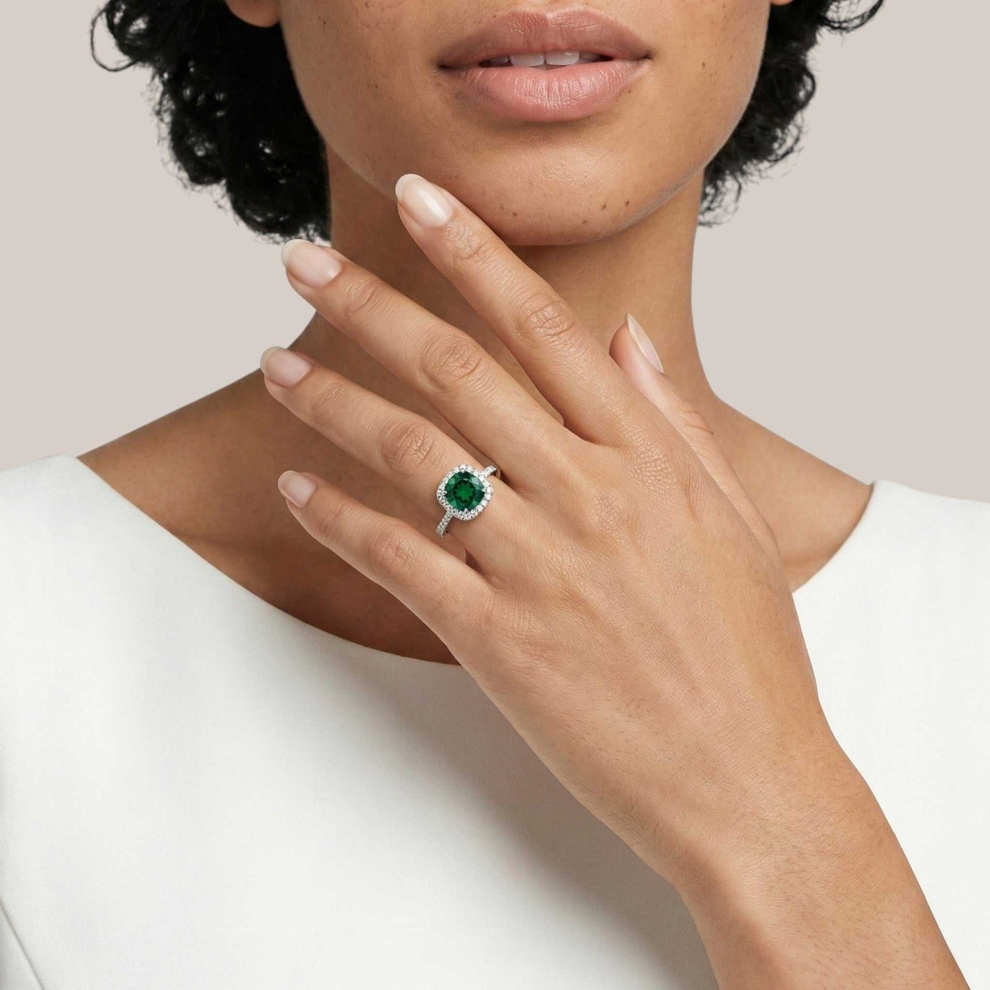 Close-up of a hand wearing an emerald ring on a neutral background