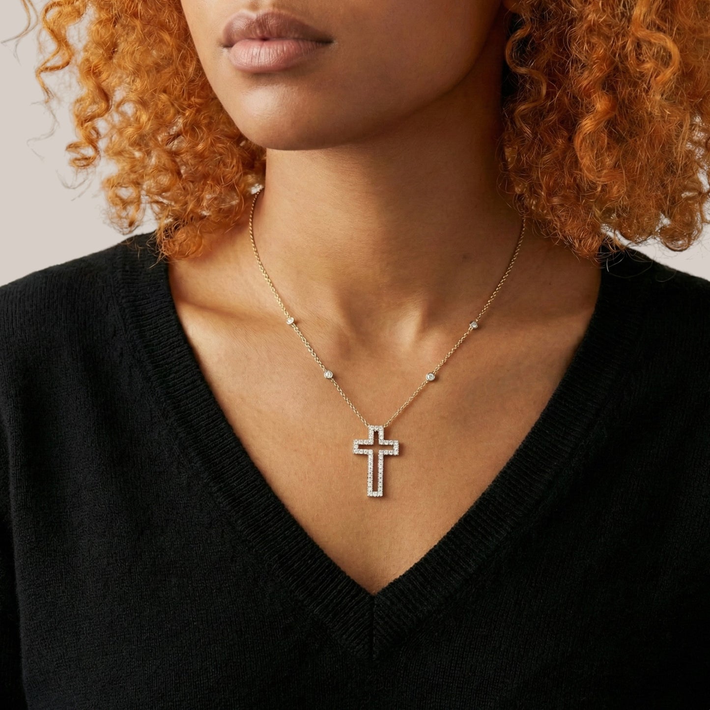 Woman wearing a gold necklace with a cross pendant against a neutral background