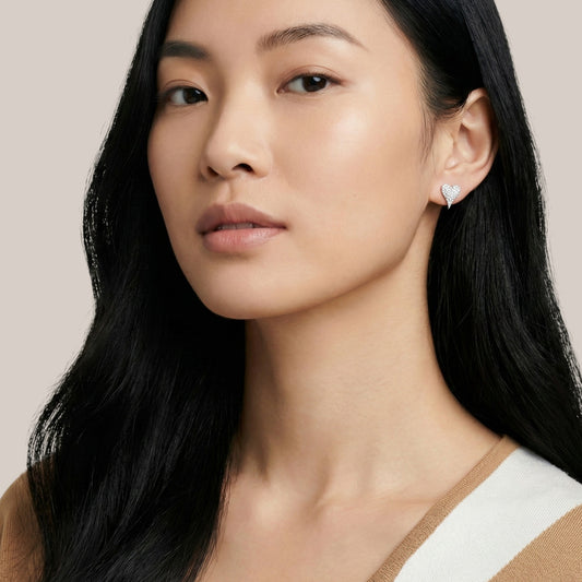 Close-up of a woman wearing a heart-shaped earring against a neutral background