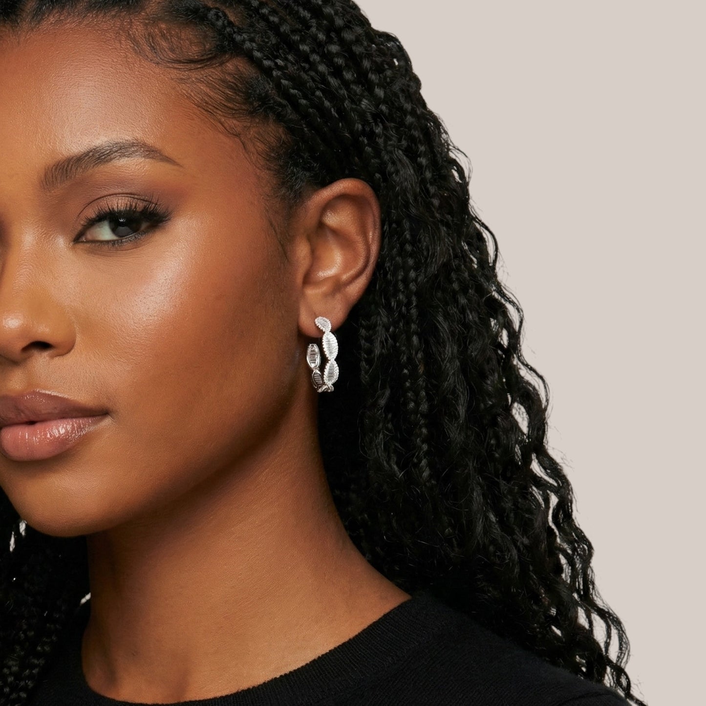 Close-up of a woman with braided hair wearing earrings against a neutral background