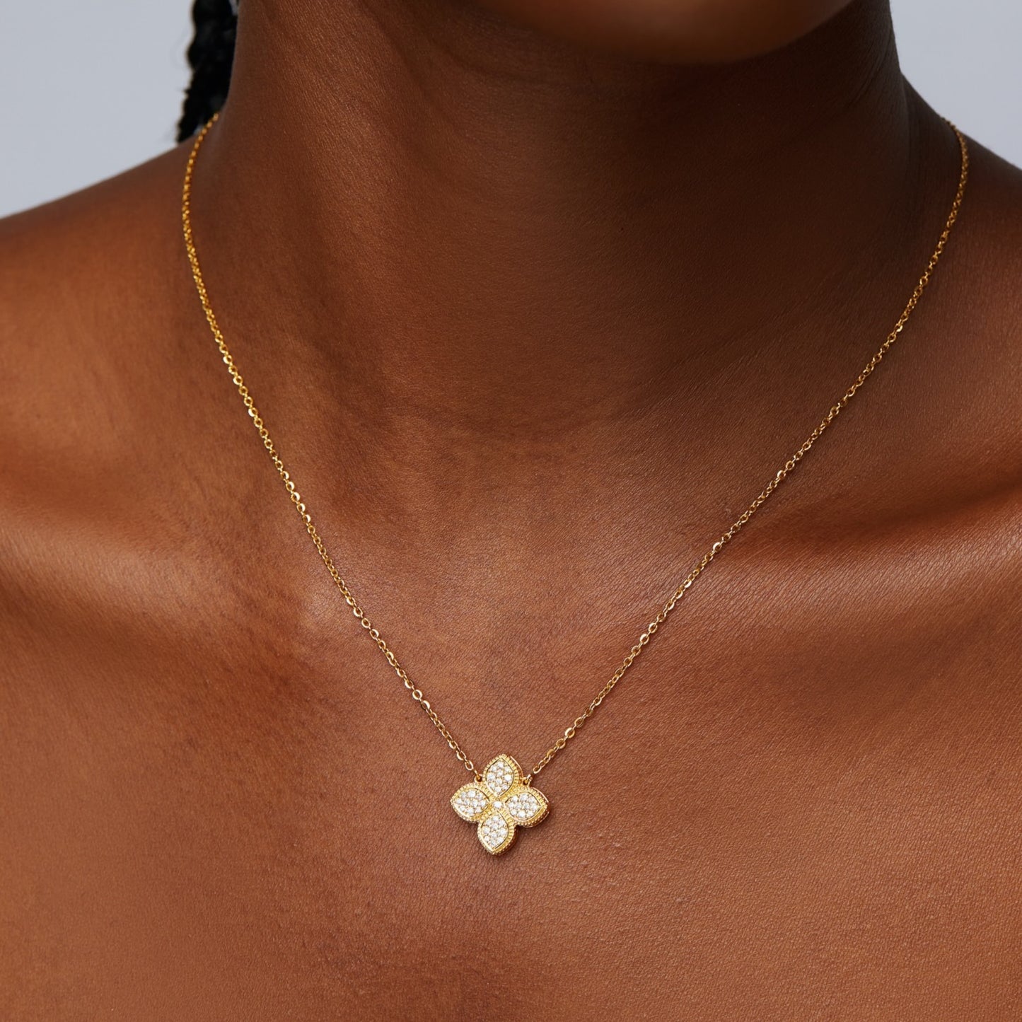 Gold necklace with a diamond-flower pendant on a person's neck against a neutral background