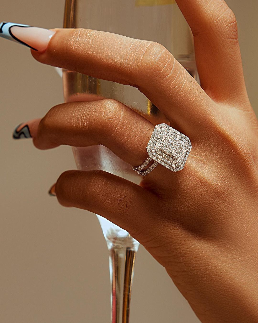 A person's hand holding a glass of champagne, with a diamond ring on the finger.
