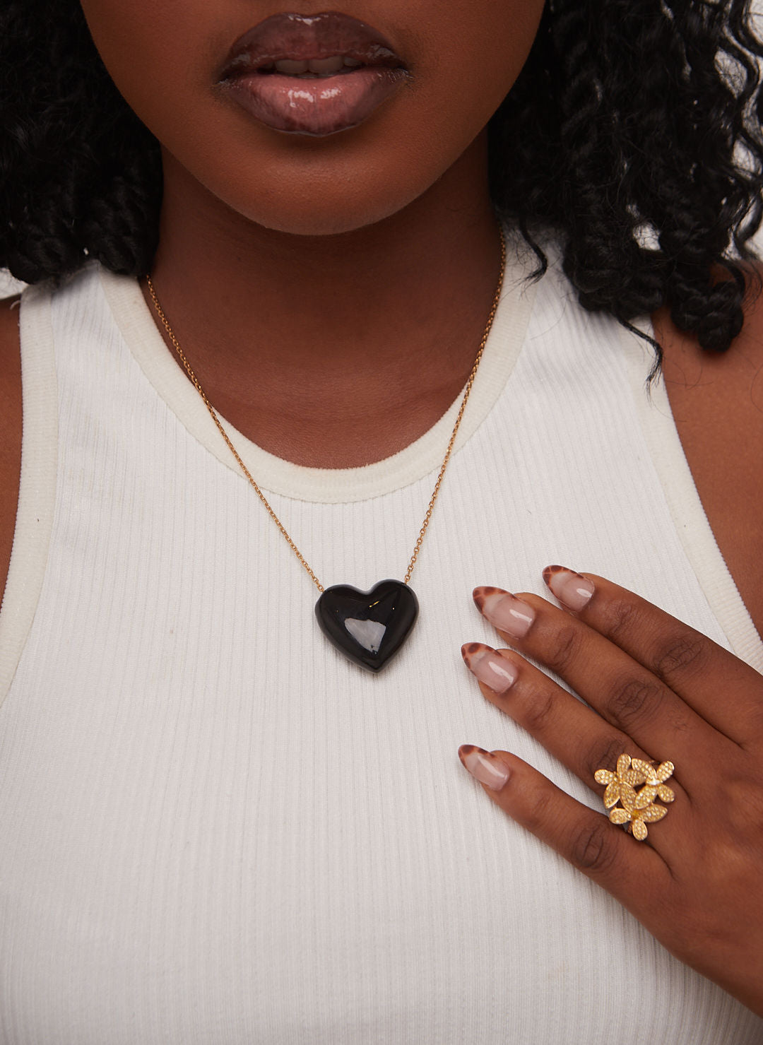 Woman wearing a necklace with a heart pendant and a gold ring on a white background