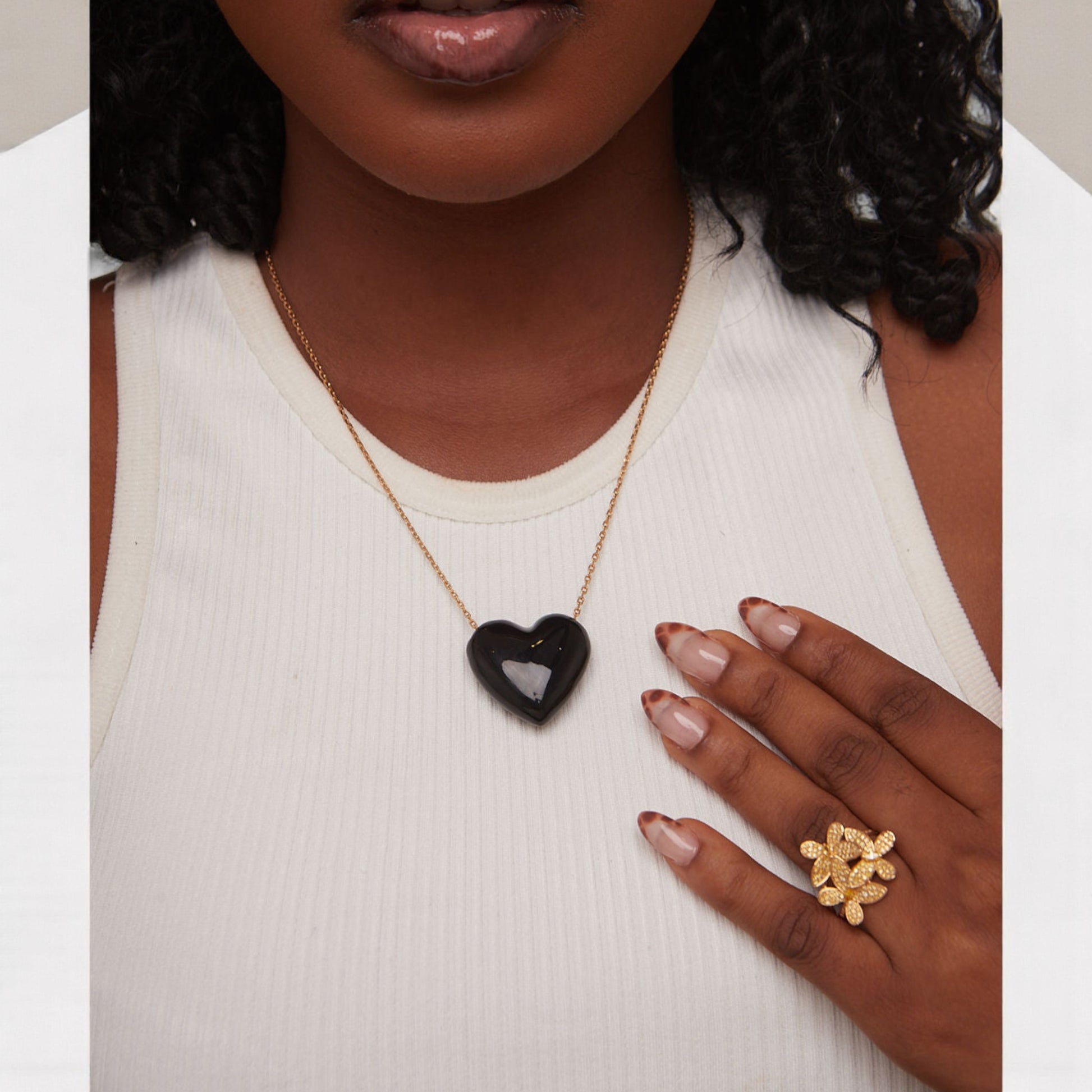 Woman wearing a gold necklace with a black heart pendant and a gold ring on her finger.