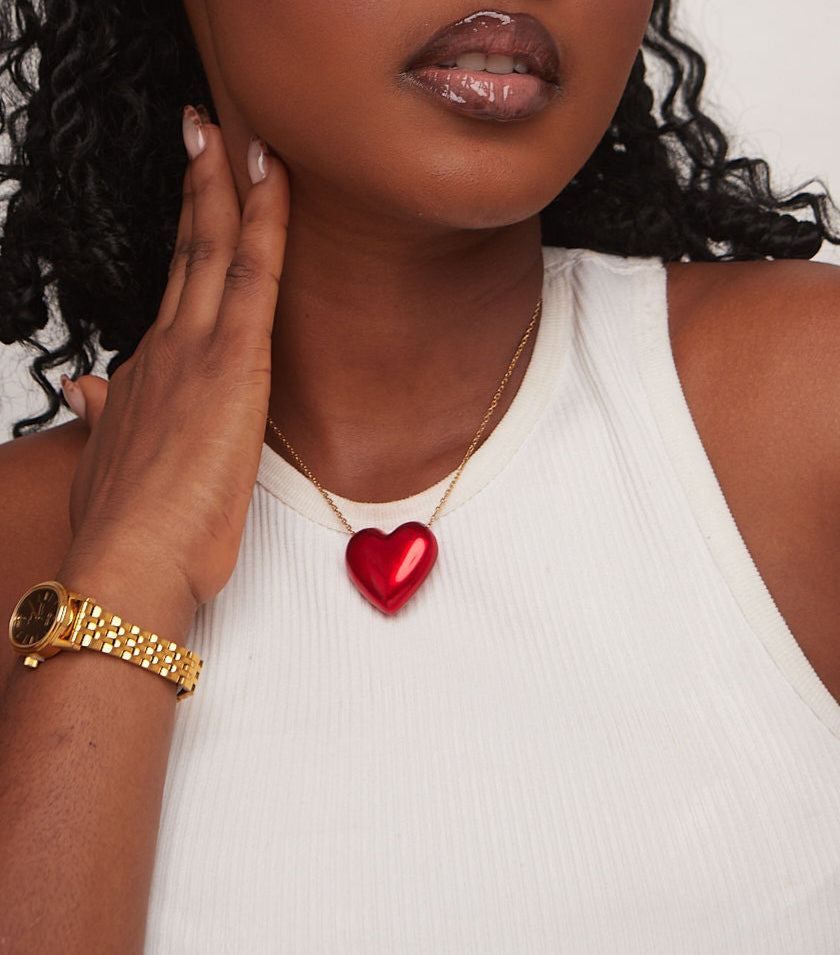 Woman wearing a gold watch and red heart necklace against a white background
