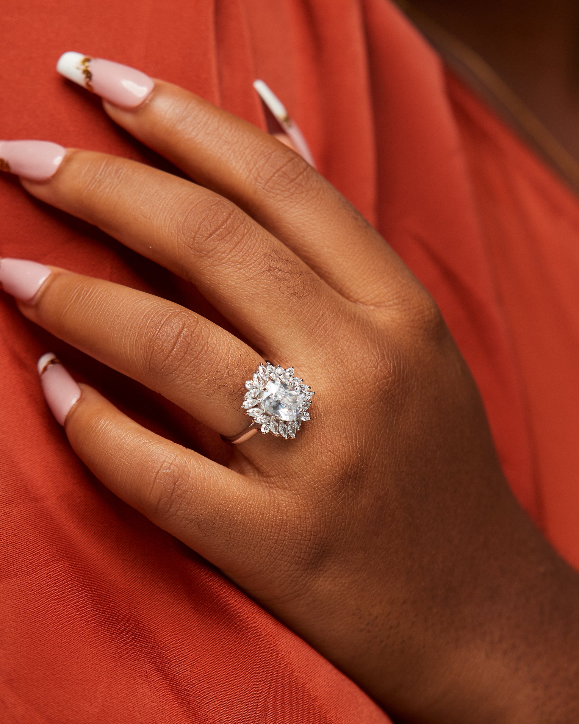 A person's hand wearing a sterling silver engagement ring with a large central cubic zirconia stone, displayed on a red background.