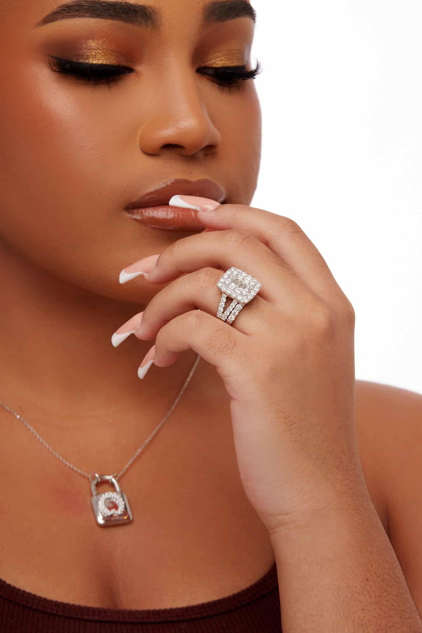 Woman wearing a silver necklace with a lock pendant and a diamond ring on a white background