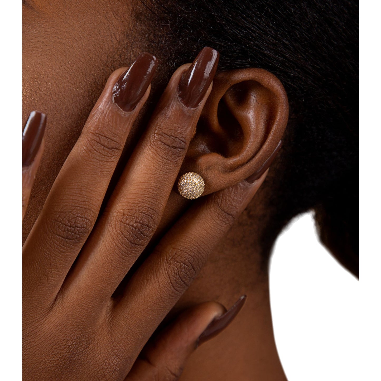 Close-up of an ear wearing a gold earring with a hand touching the earlobe.