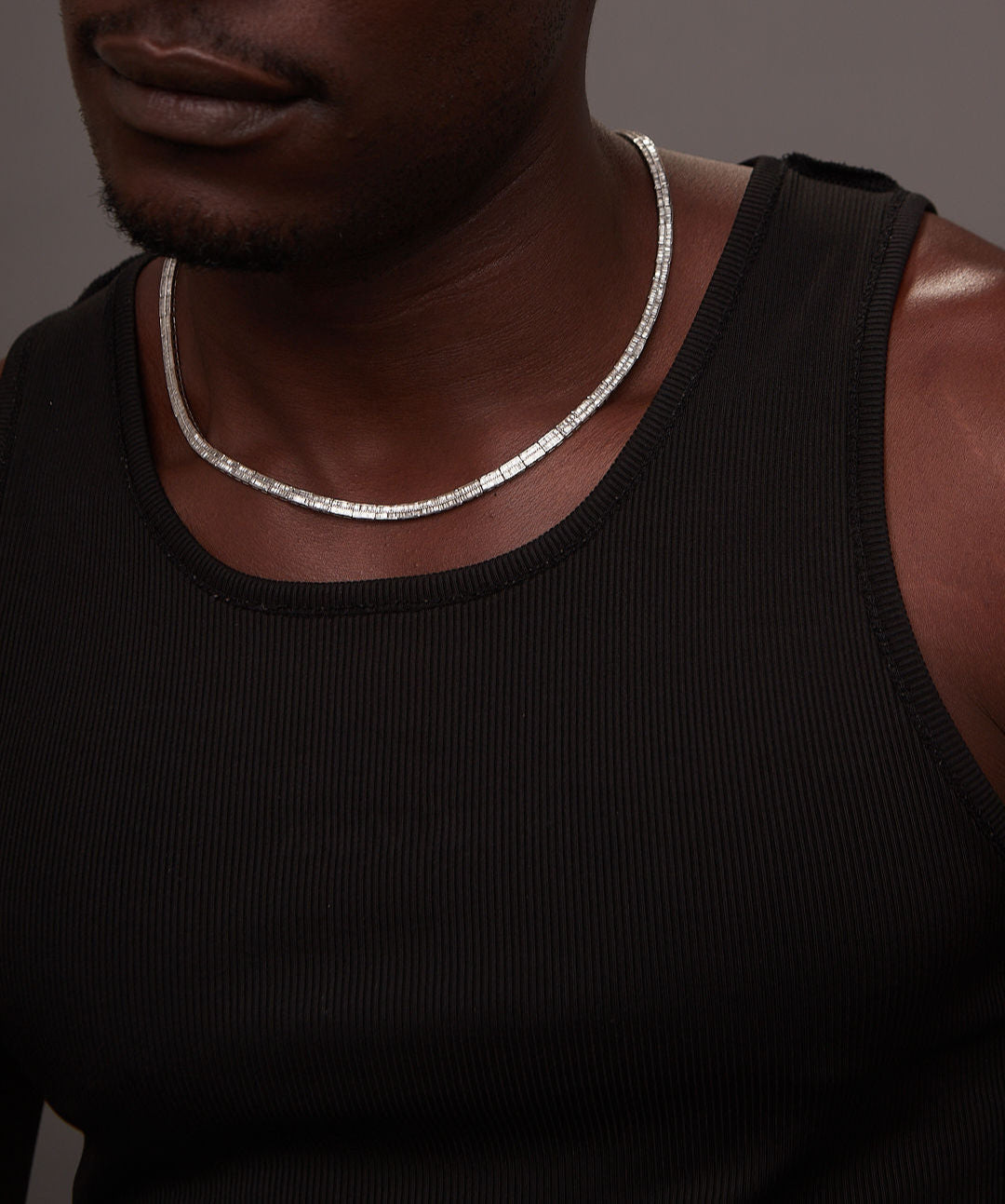 Man wearing a black tank top and silver necklace against a dark background
