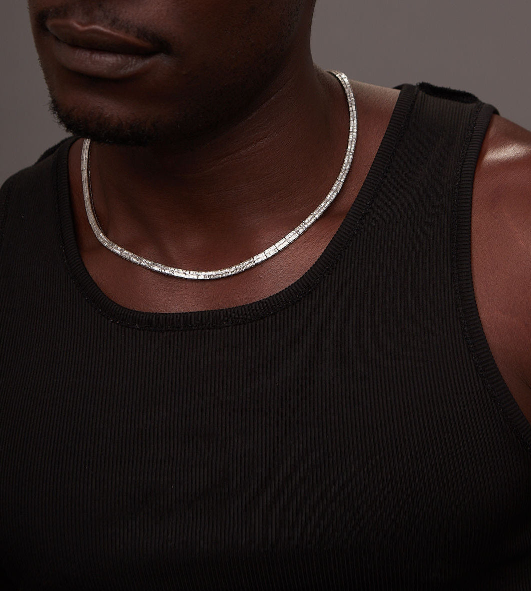 Man wearing a black tank top and silver necklace against a dark background