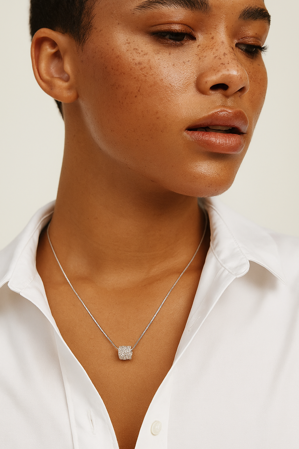 Woman wearing a silver necklace with a white shirt on a neutral background