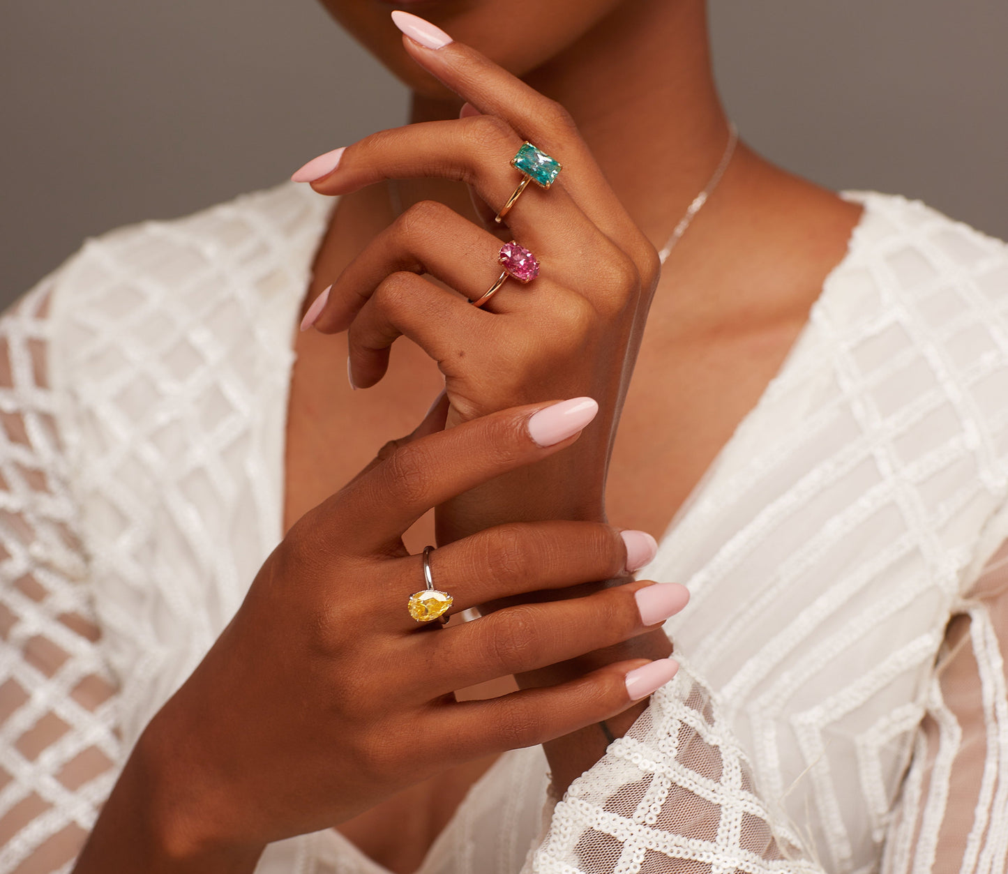 Close-up of a person's hand wearing multiple rings with a neutral background