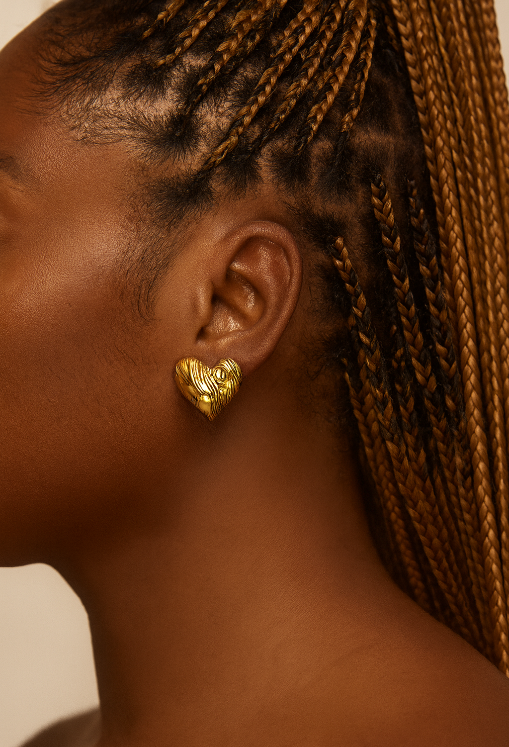 Close-up of an ear wearing a gold heart-shaped earring with braided hair.