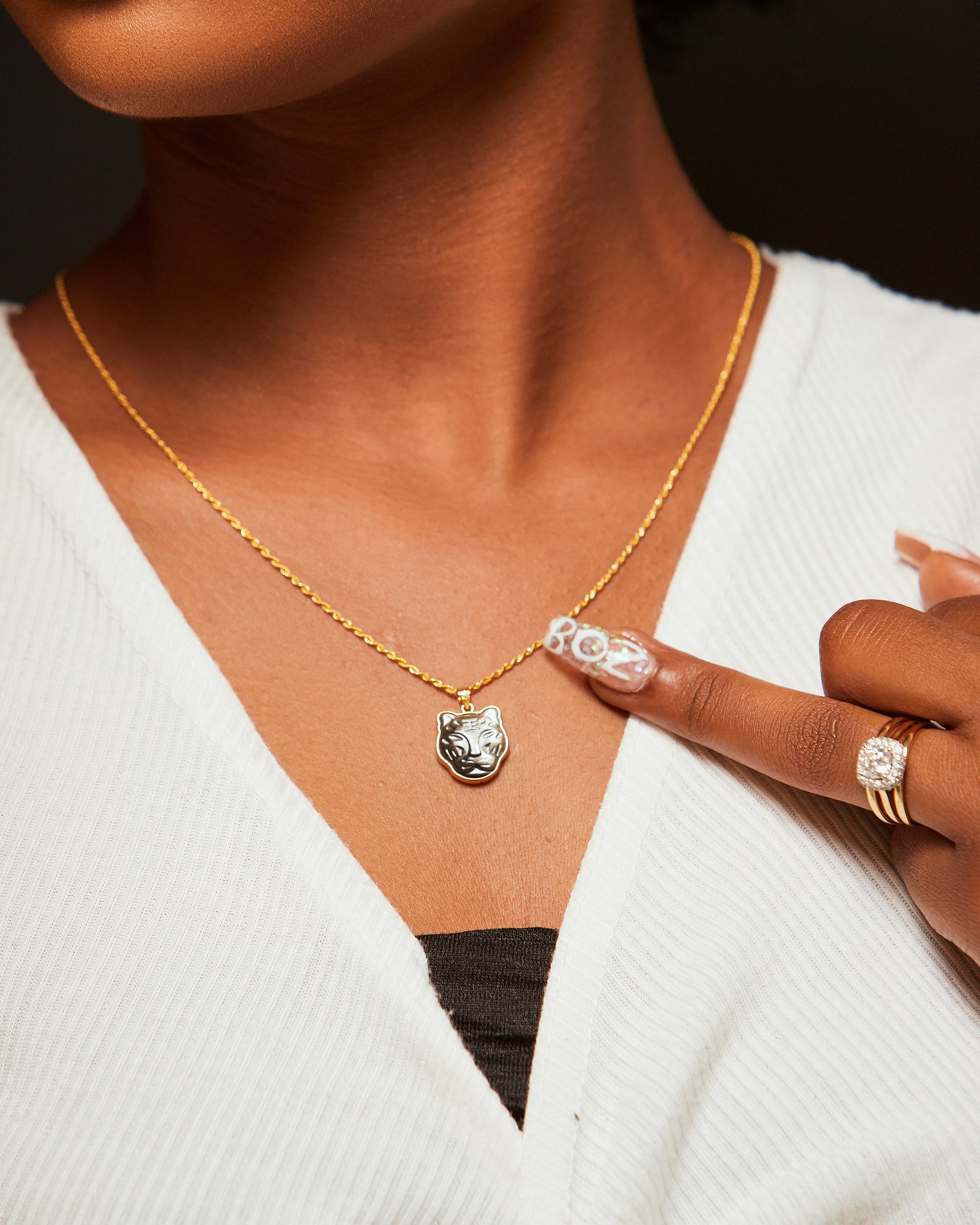 A person wearing a white cardigan has a Black Panther pendant necklace in 18K gold displayed on their neckline.