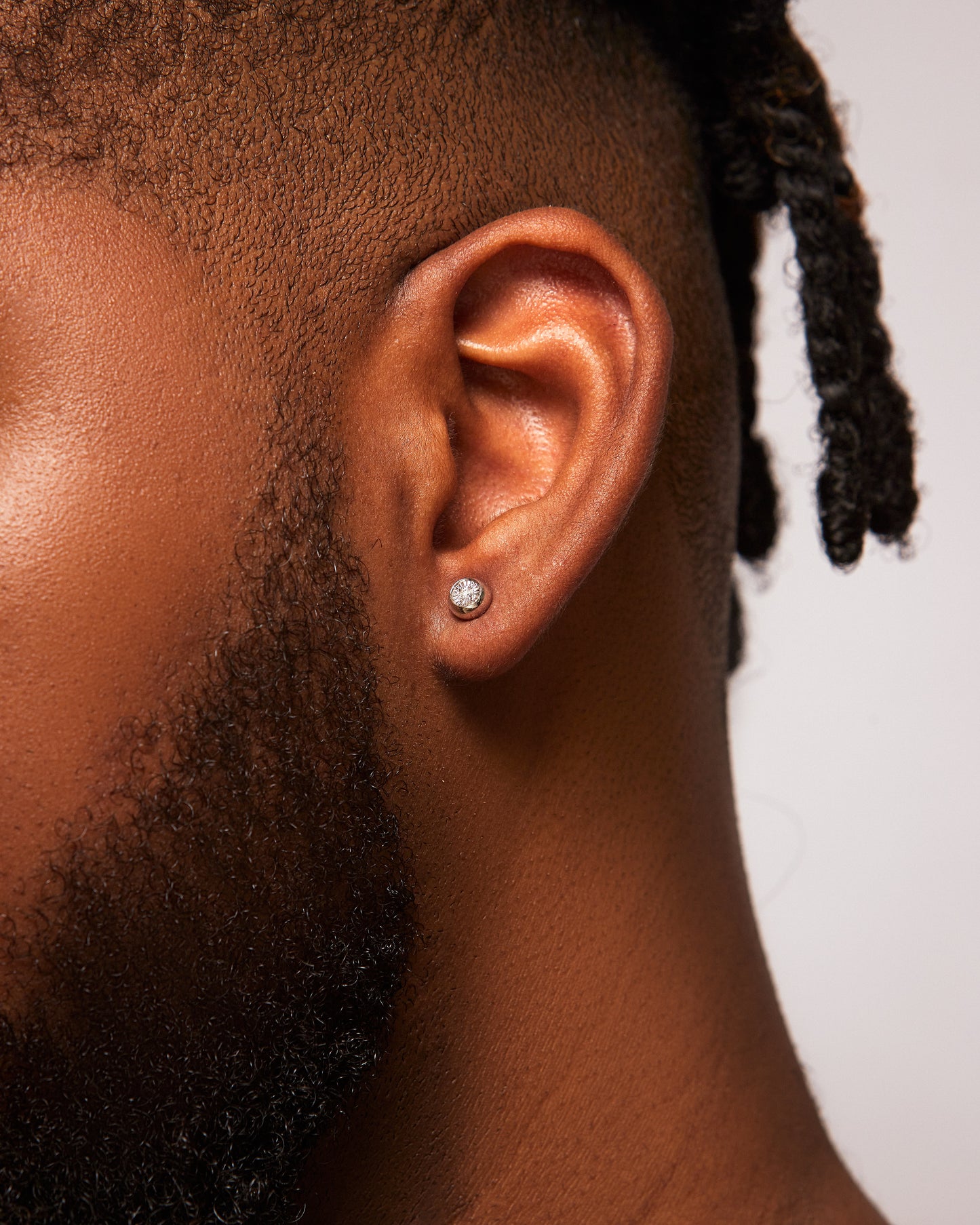 Close-up of an ear with a diamond earring on a neutral background