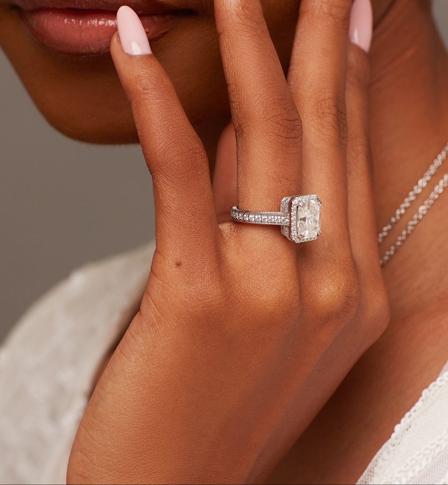 A person's hand displaying an 18 karat gold engagement ring with a moissanite gemstone on their finger.