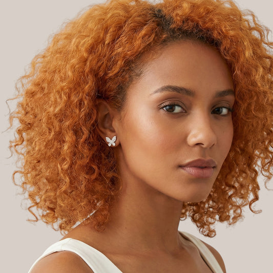 Woman with curly orange hair wearing a butterfly earring on a light background