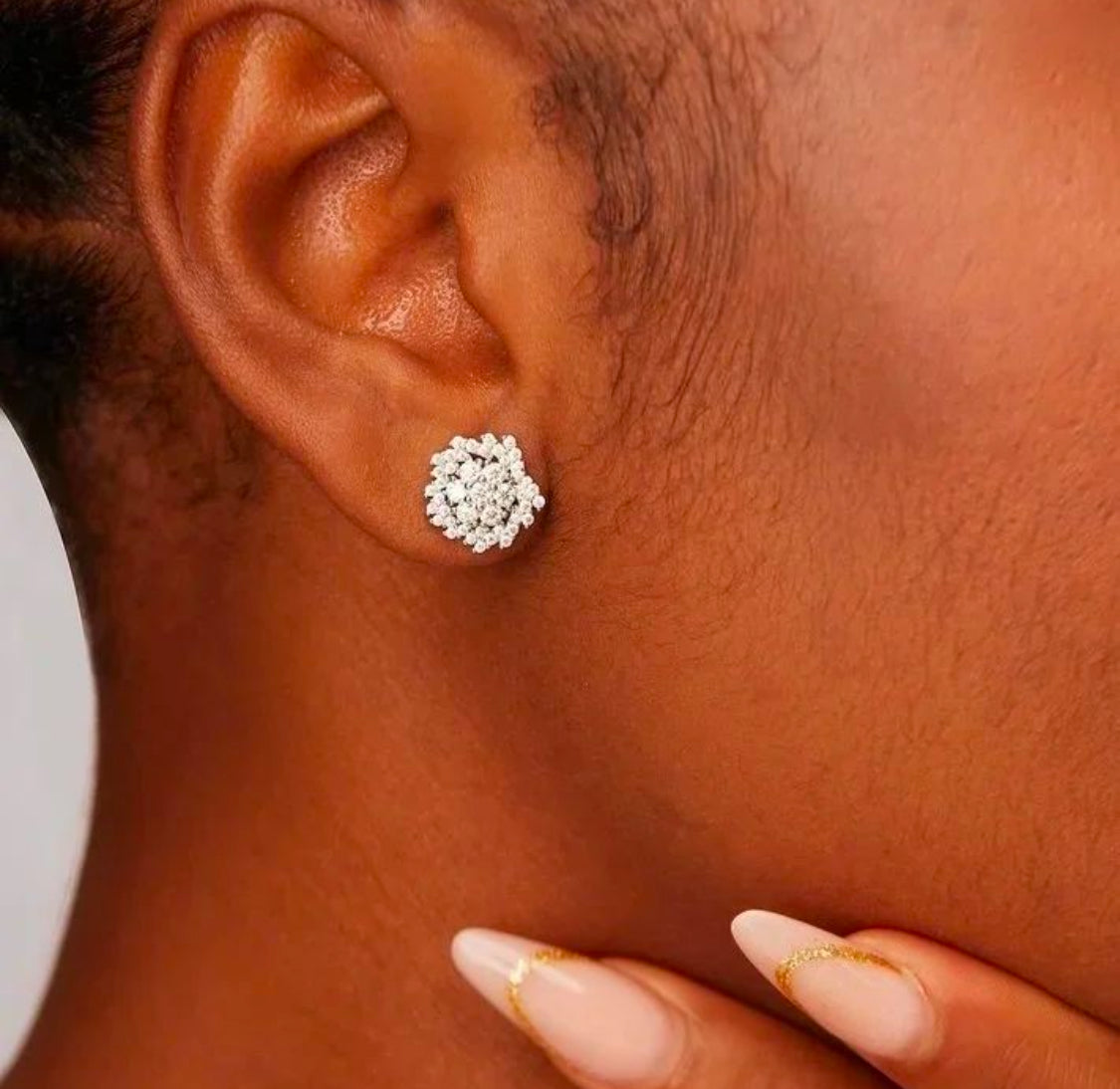 A close-up image of a person's ear wearing a moissanite stud earring, with the rest of the ear and part of the neck visible.