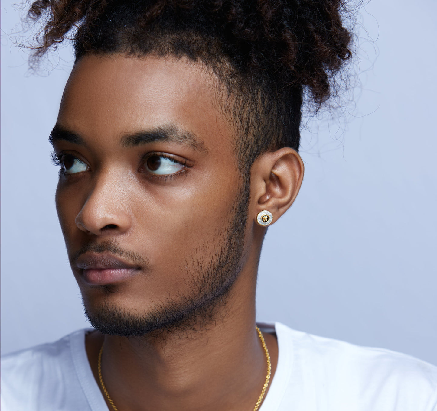 Man wearing a gold earring and necklace against a light purple background
