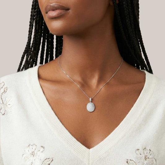 Woman wearing a silver necklace with a pendant against a neutral background
