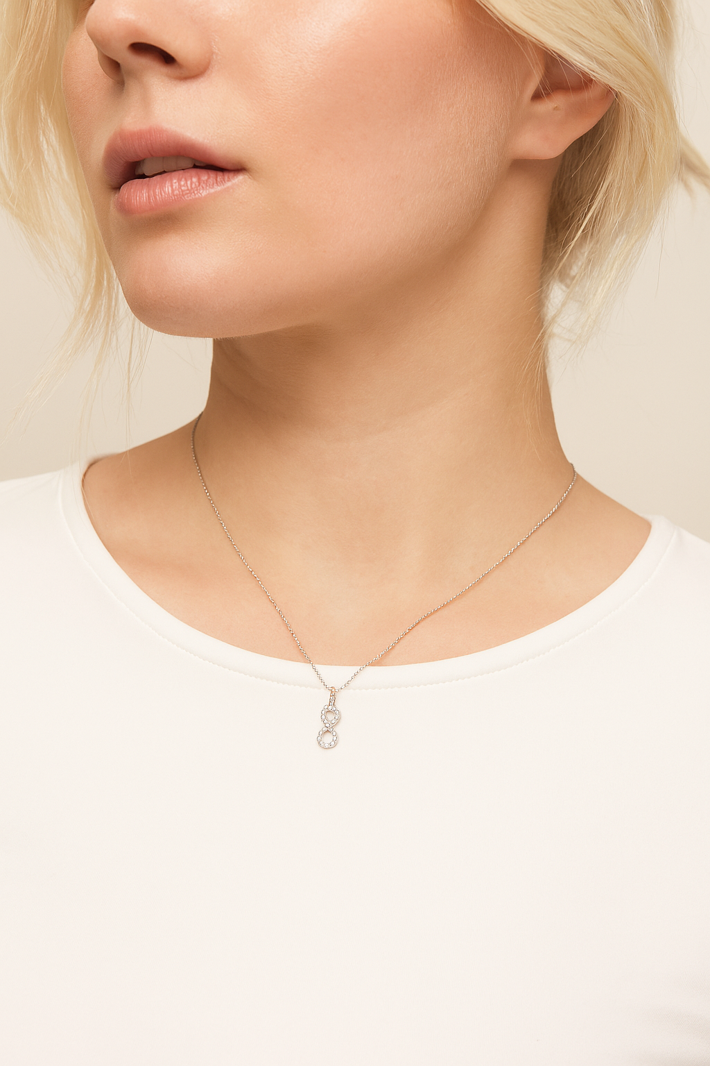 Close-up of a person wearing a delicate necklace with a small pendant on a plain background