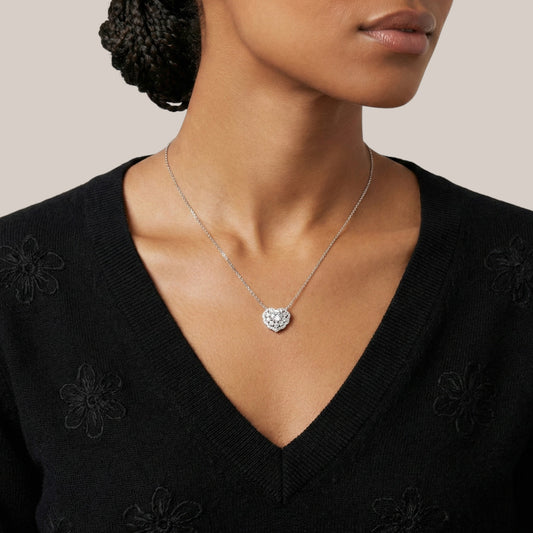 Woman wearing a black top with floral details and a silver heart-shaped necklace.