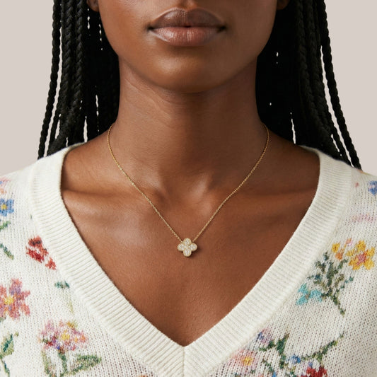 Woman wearing a gold necklace with a clover pendant against a neutral background