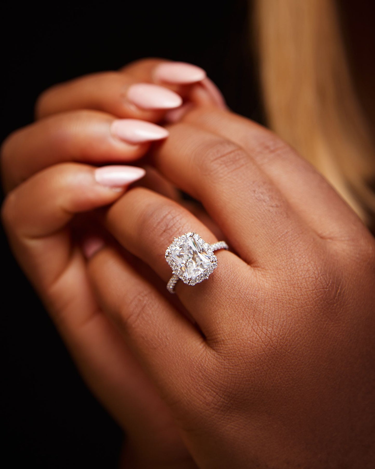 A person's hand holding a sterling silver engagement ring with a clear, polished band and a prominent, sparkling blue stone.