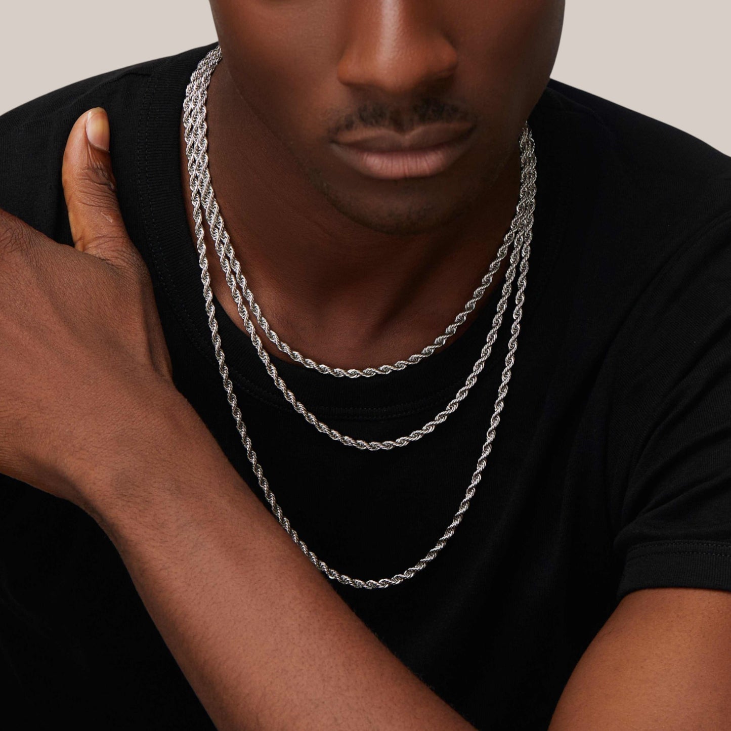 Man wearing a silver chain necklace with a neutral background