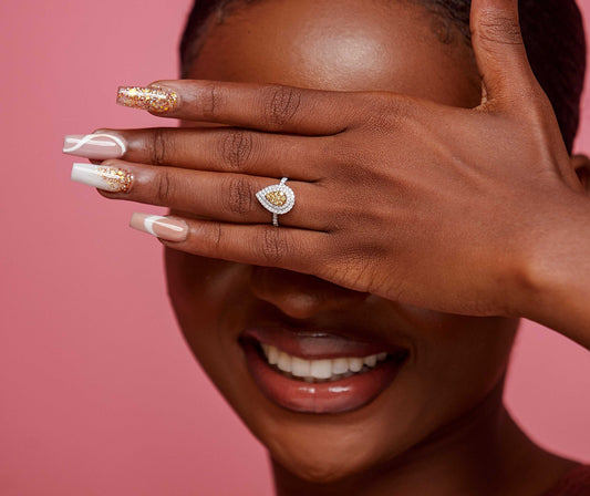 A person showcasing an 18 karat gold engagement ring with a pear cut natural diamond on their finger.