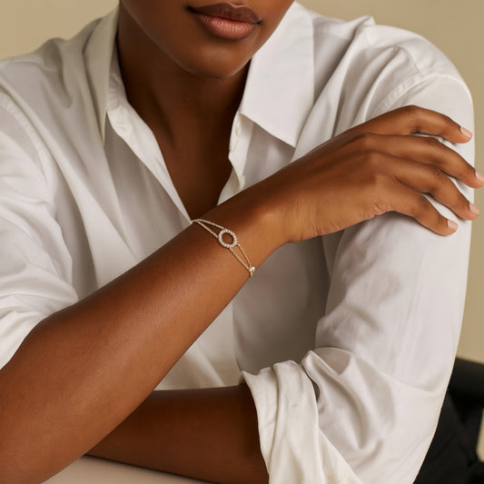 Person wearing a gold bracelet with a circular design on a neutral background