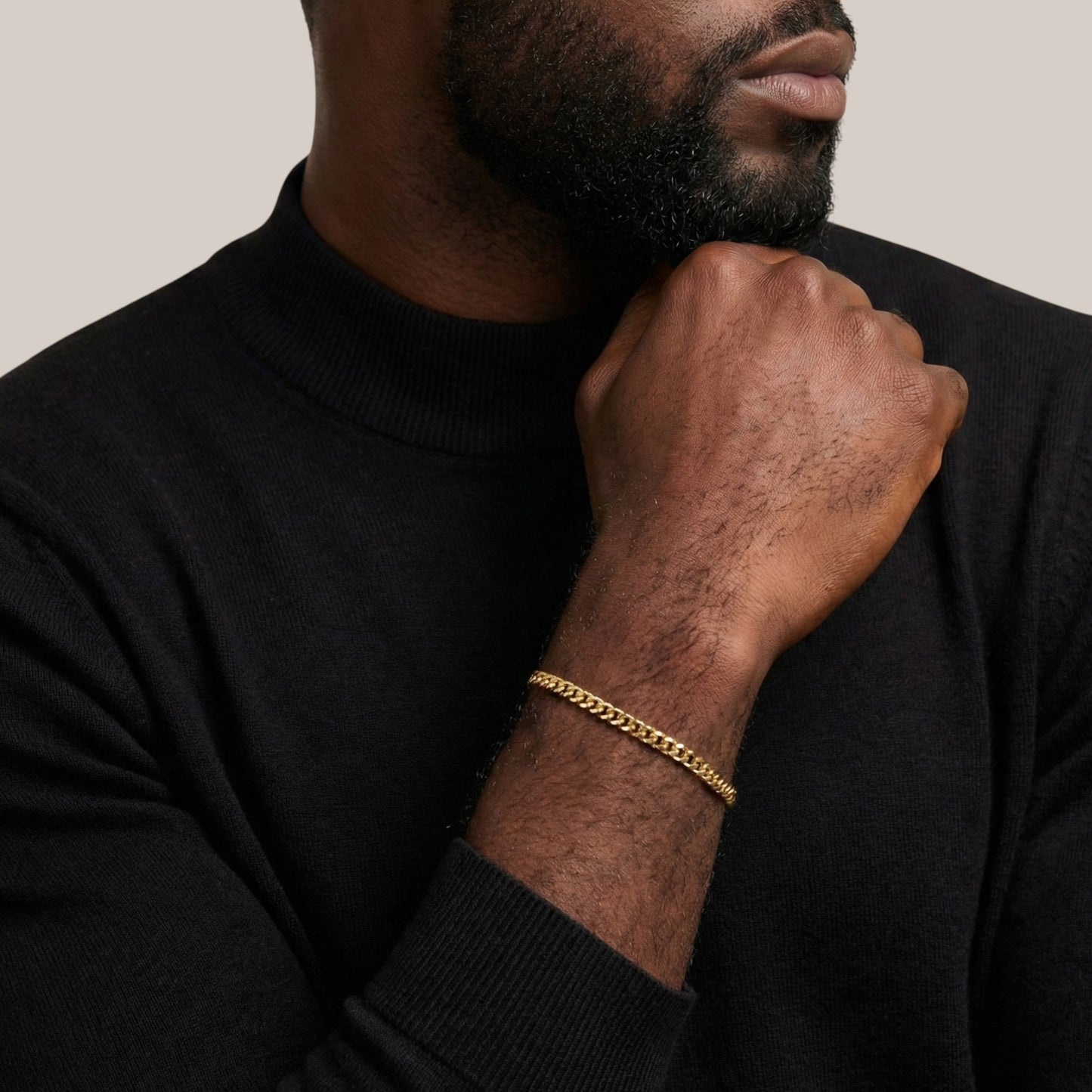 Man wearing a black sweater and gold bracelet on a neutral background