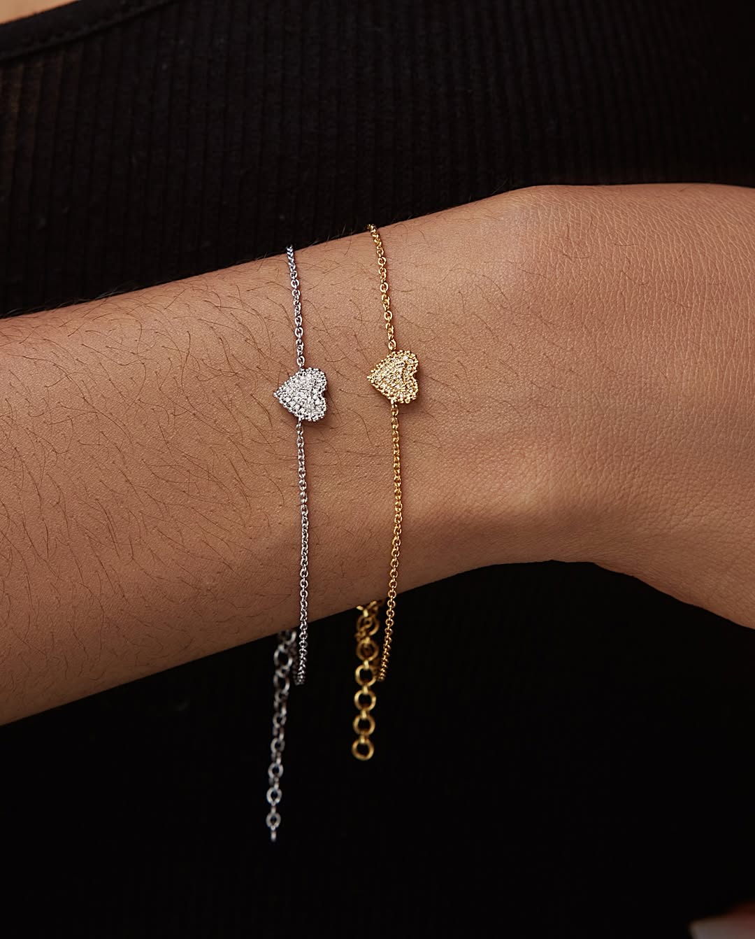 Two bracelets on a person's wrist, one in 18K gold with natural diamonds, and the other in a different metal with a chain-link design.
