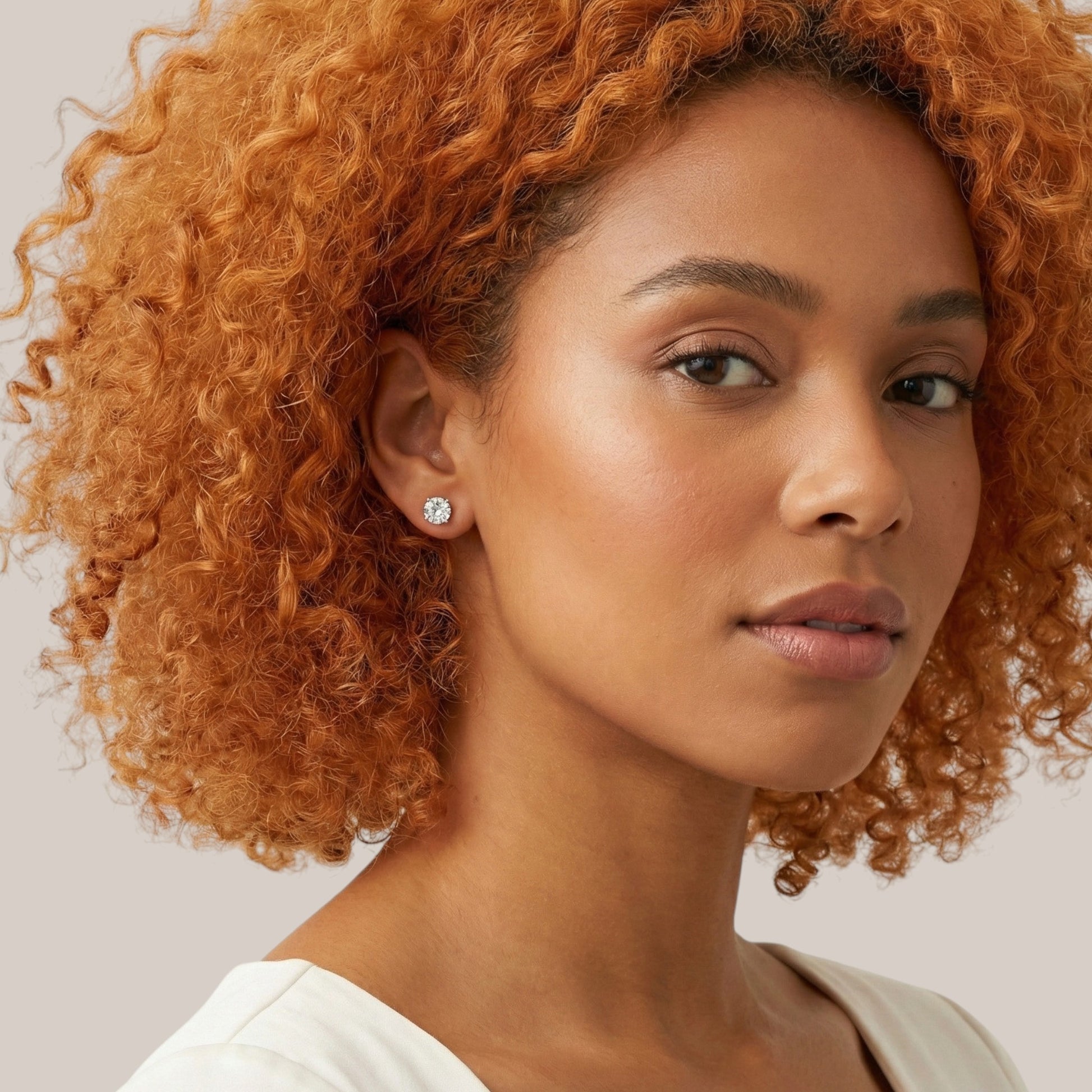 Woman with curly hair wearing a diamond earring on a neutral background