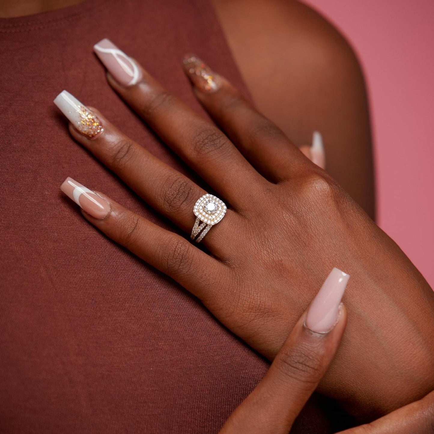Hand wearing a diamond ring on a pink background