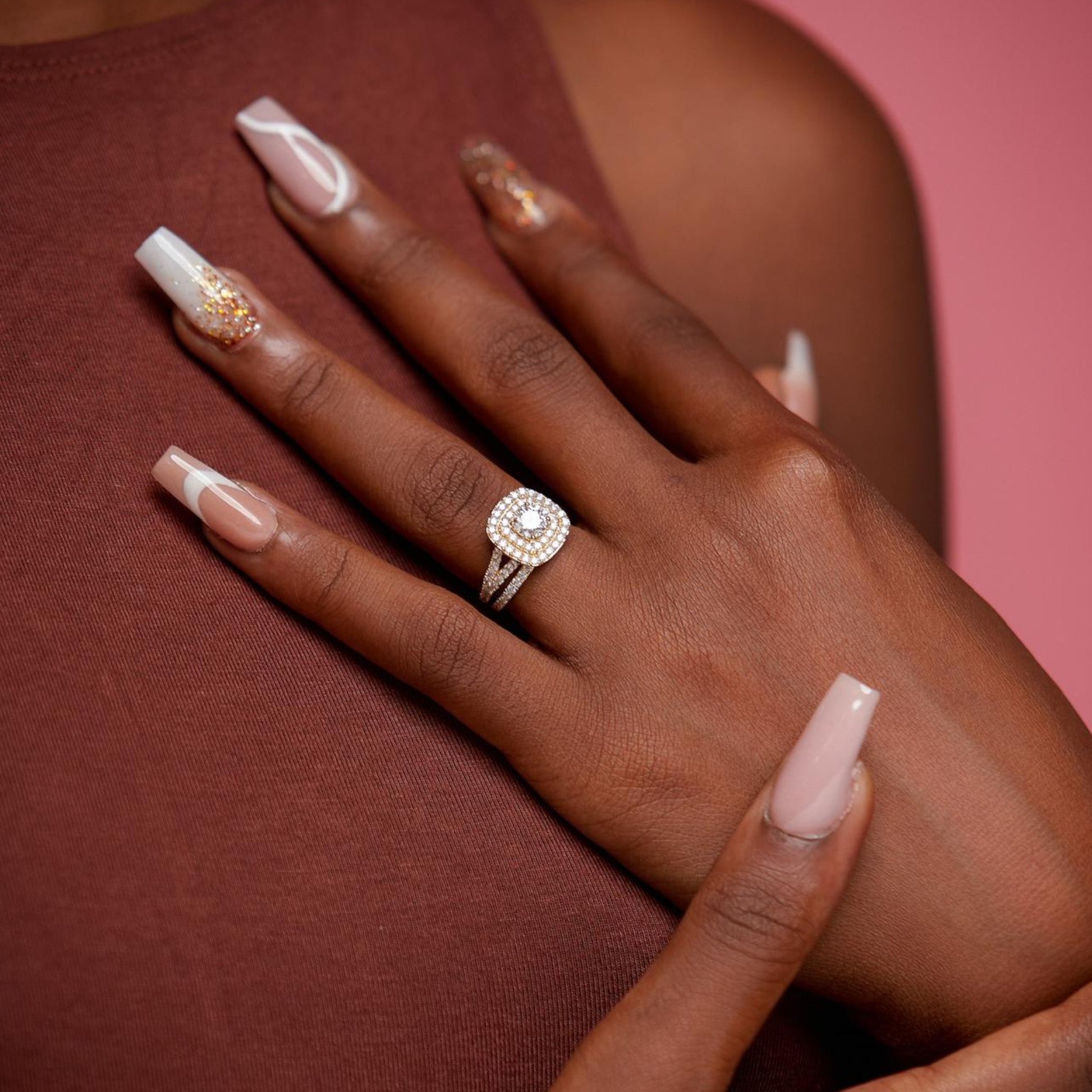 Hand wearing a diamond ring on a pink background