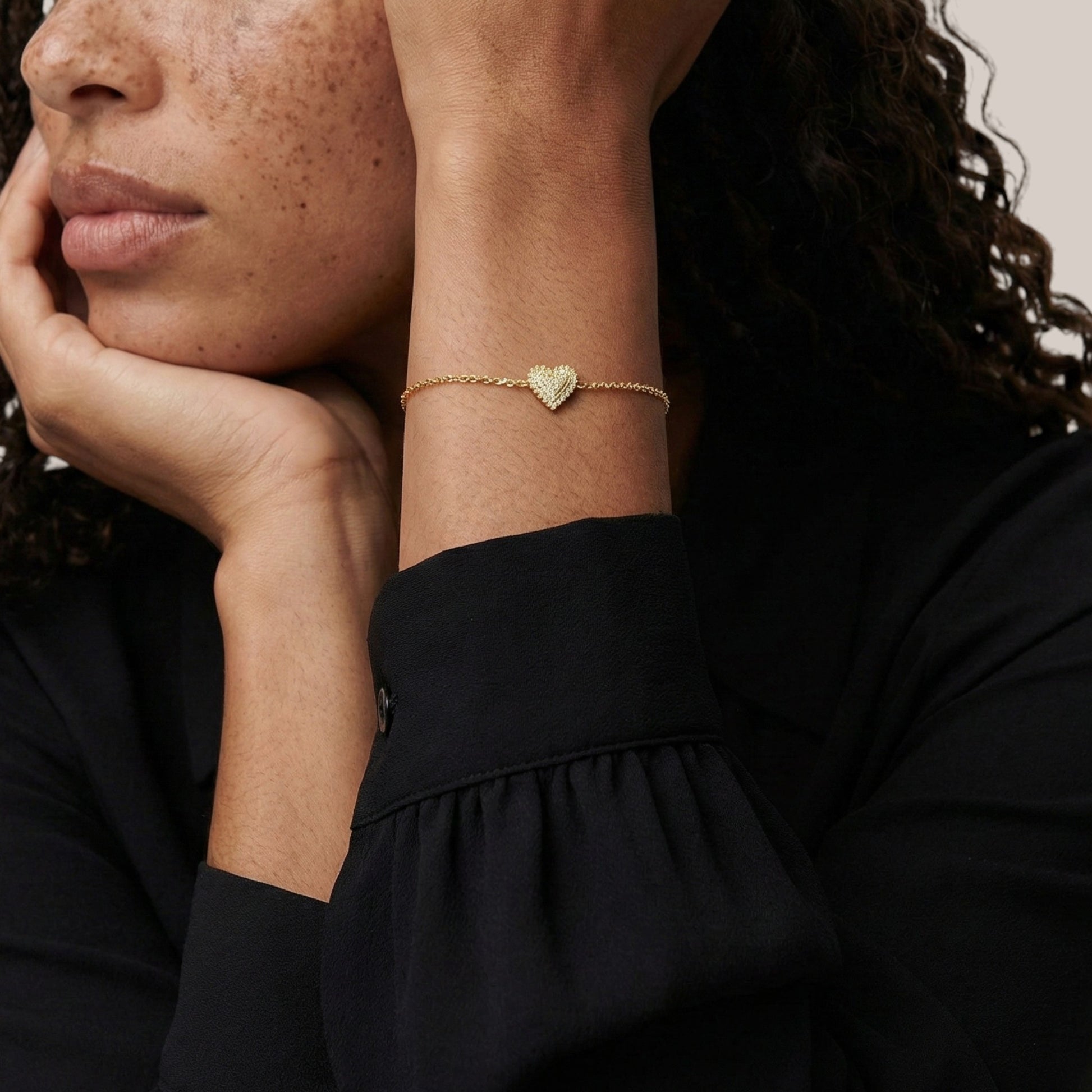 Close-up of a woman wearing a gold bracelet with a heart charm on her wrist.