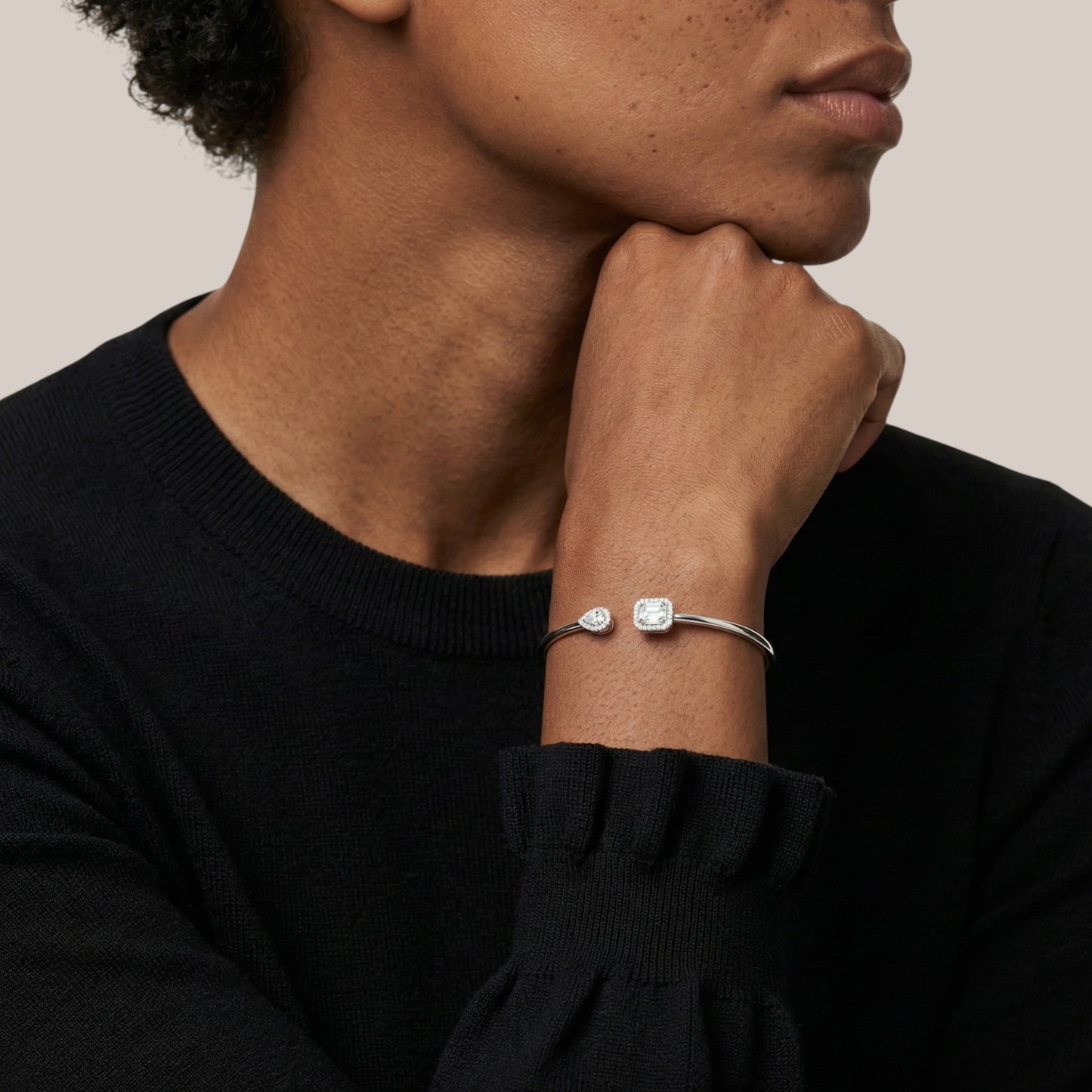 Person wearing a silver bracelet with a clear gemstone on a neutral background