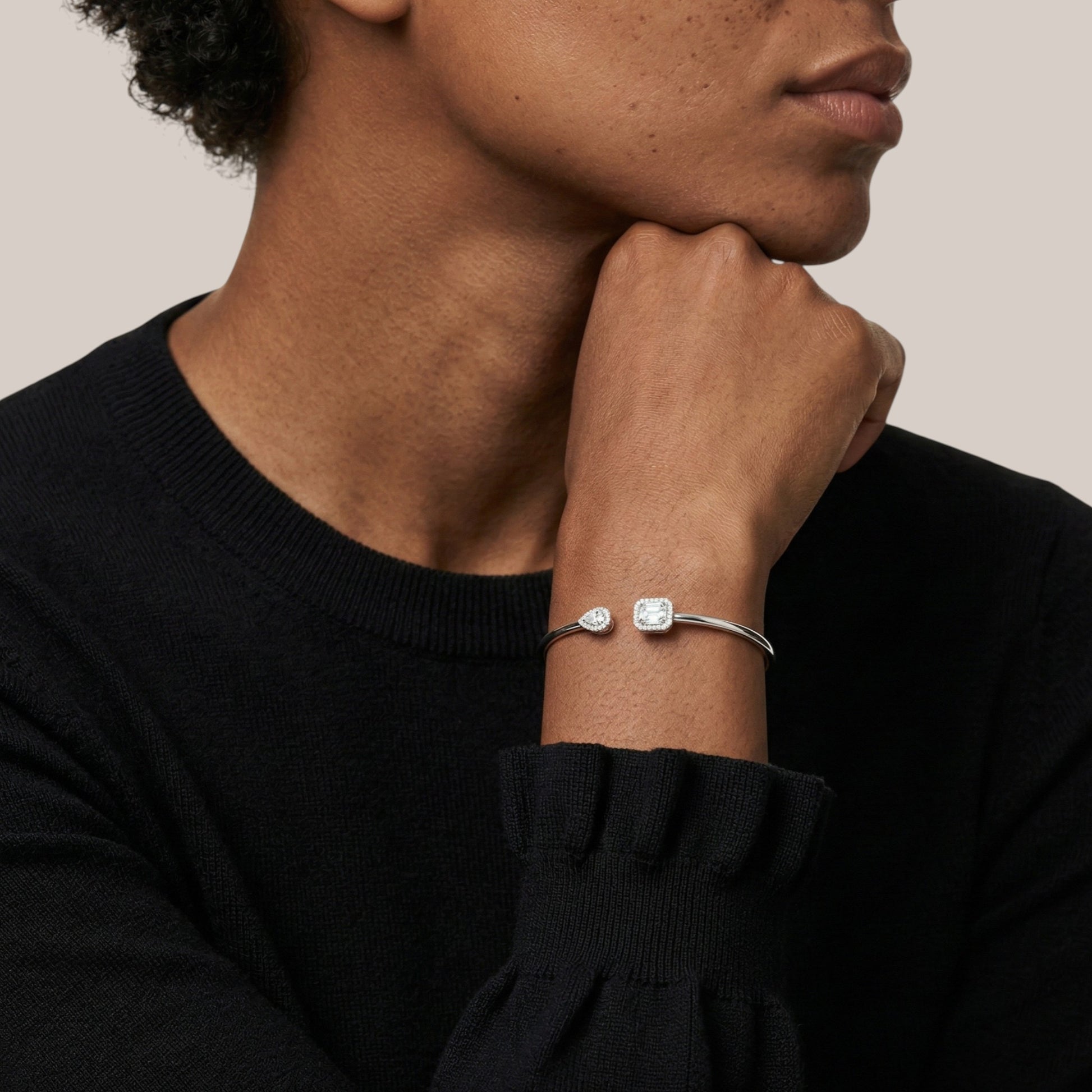 Person wearing a silver bracelet with a clear gemstone on a neutral background