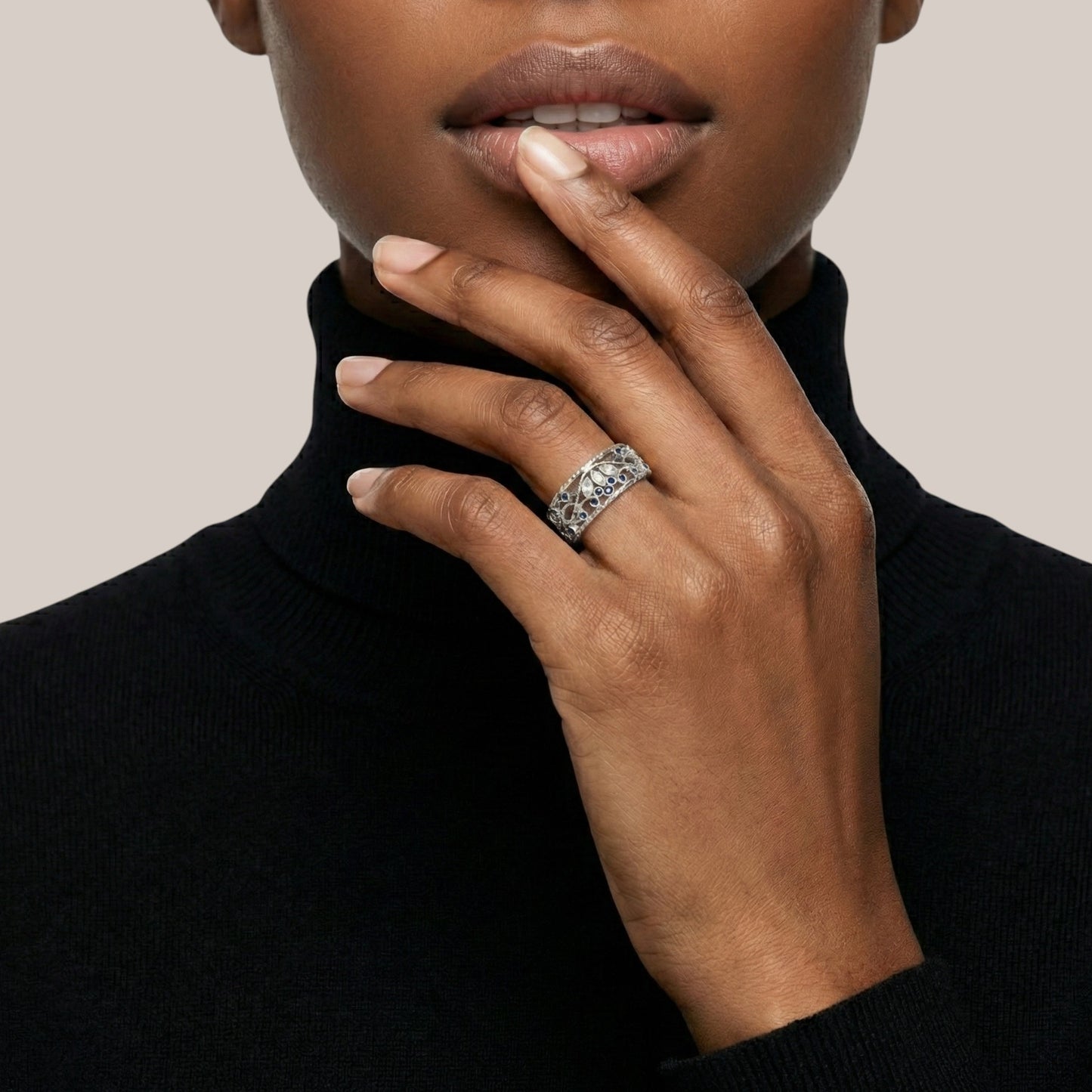 Close-up of a person wearing a black turtleneck and a ring on a neutral background