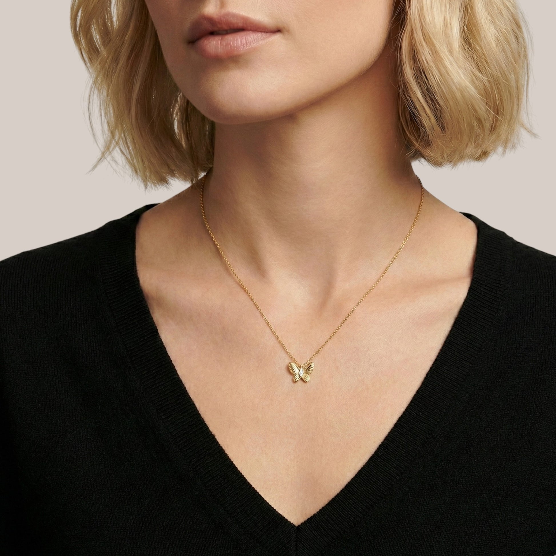 Gold necklace with a butterfly pendant worn by a person against a neutral background