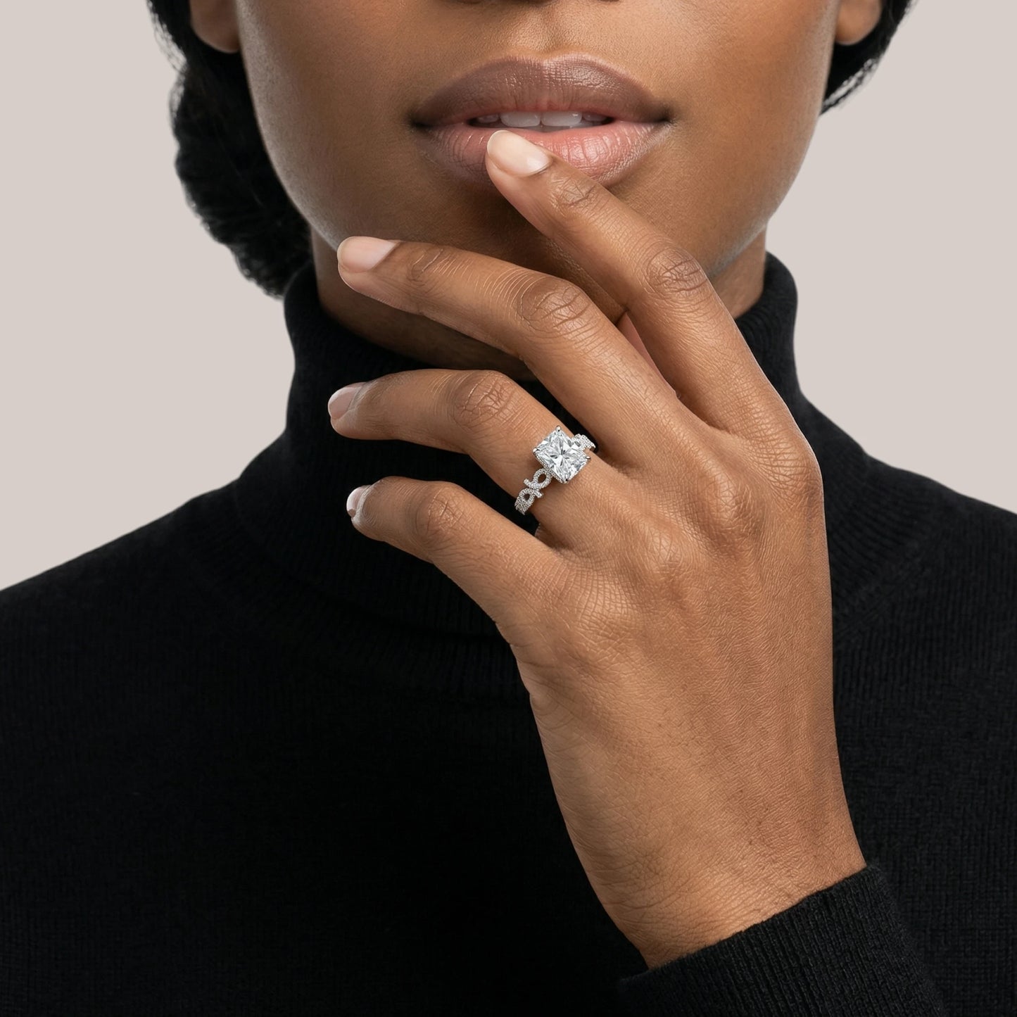Close-up of a hand wearing a ring with a diamond, touching the chin against a neutral background