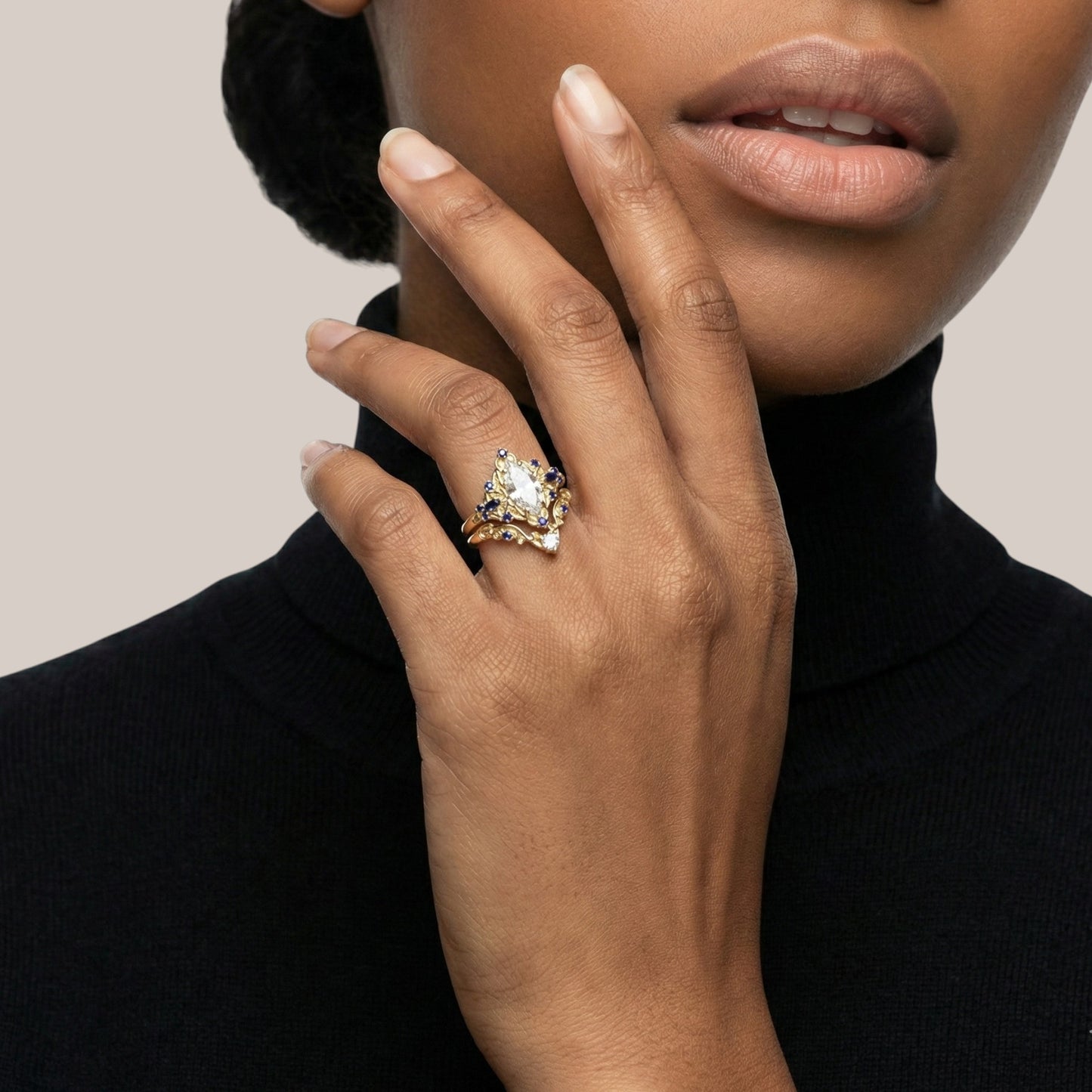Hand wearing a gold ring with a large gemstone against a neutral background
